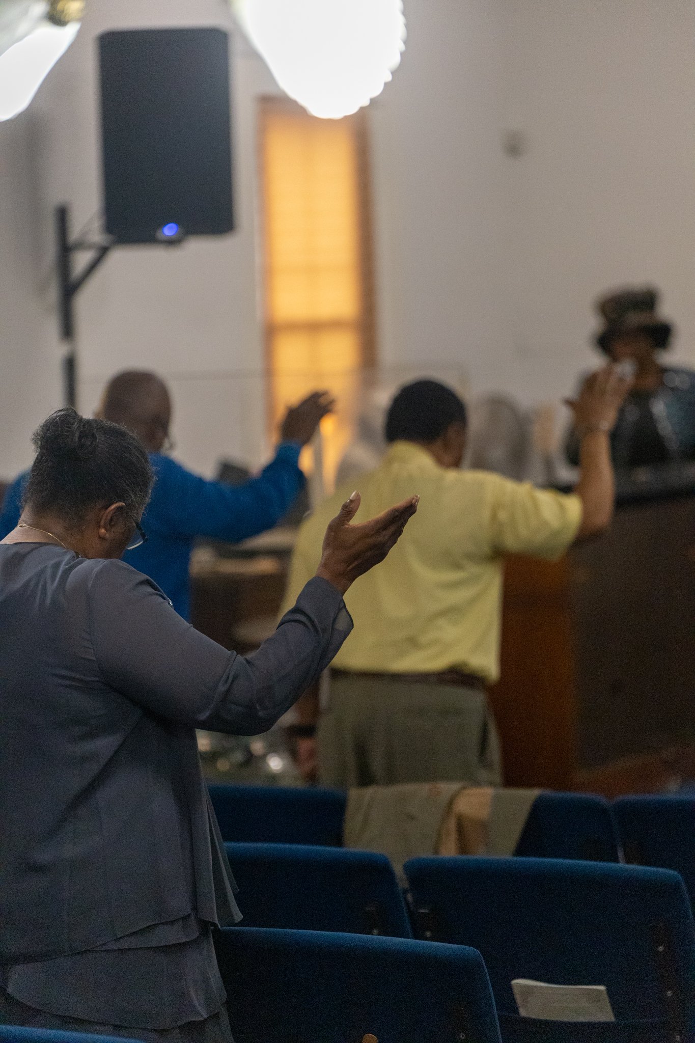 People worshiping with raised hands in a church interior with blue pews and warm lighting