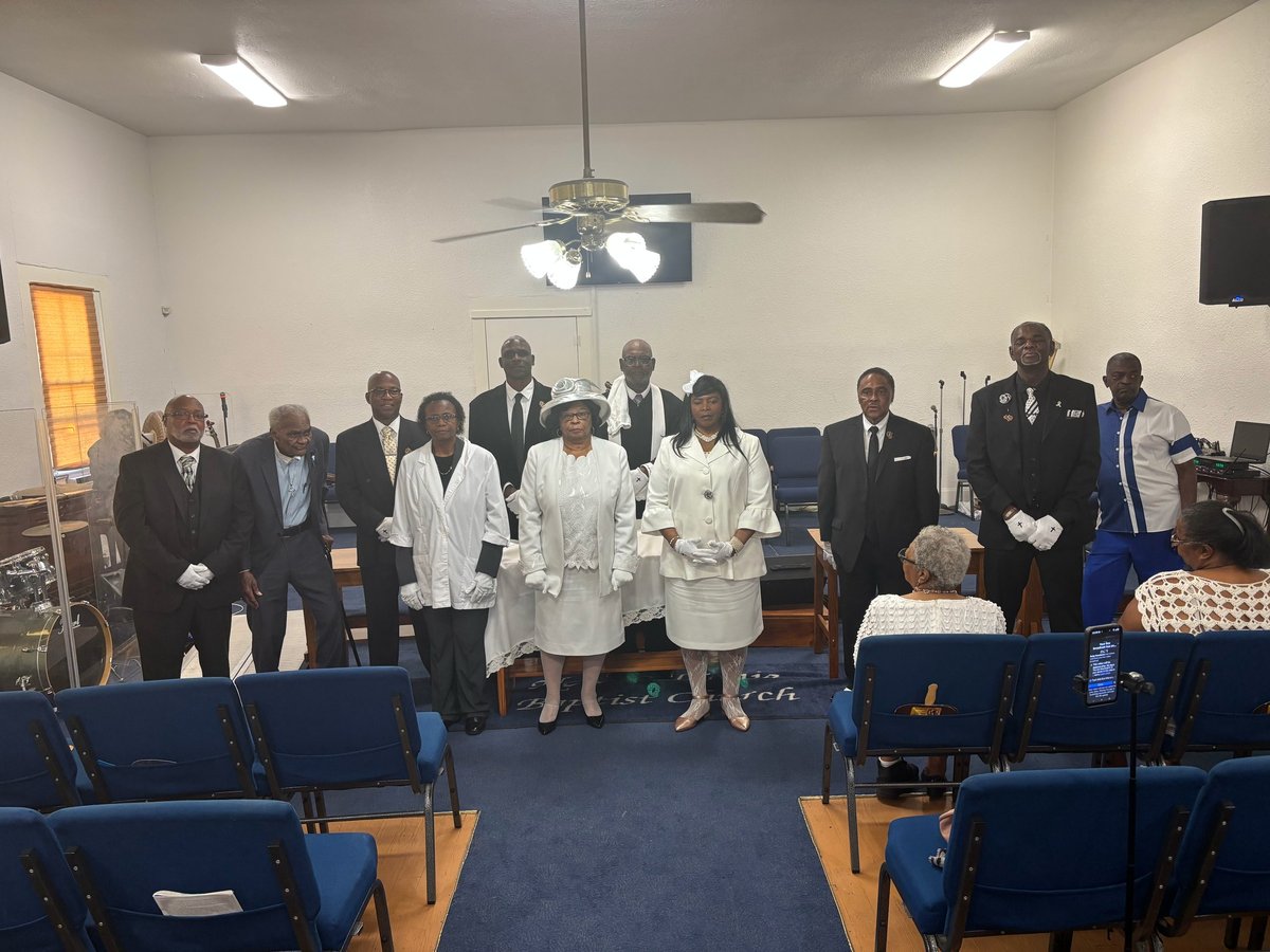 Group of formally dressed people standing in a row inside a church or chapel during what appears to be a ceremonial service or ordination